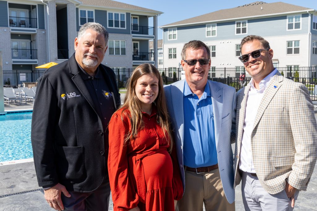 Arlington Farms RC 572026 FS-12 - Extol Media Four adults stand together by a swimming pool at a modern apartment complex.