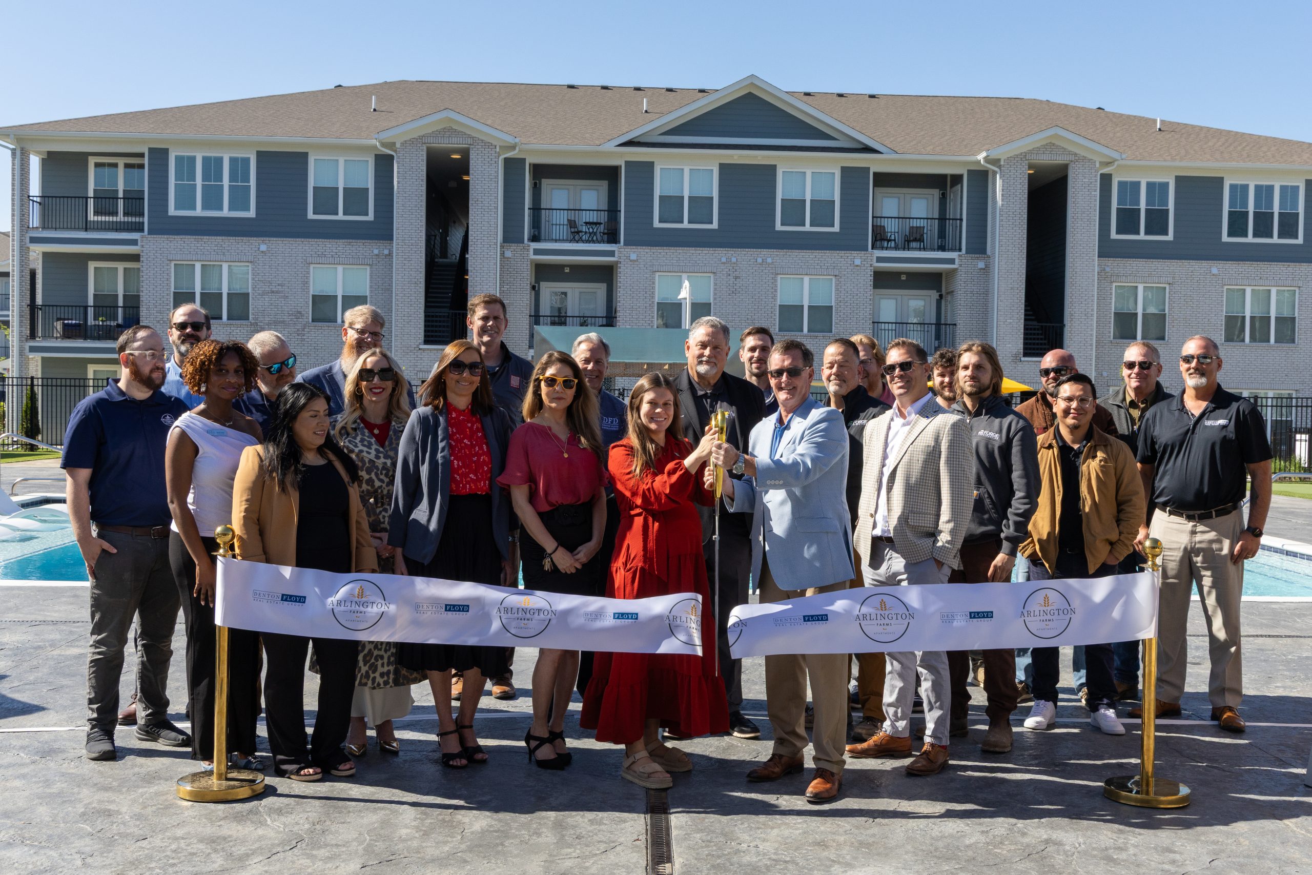 Diverse group of adults at a ribbon-cutting ceremony outside a modern apartment complex.