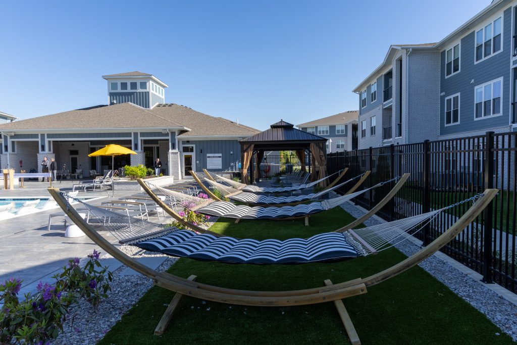 Arlington Farms RC 572026 FS-99 - Extol Media Poolside courtyard with striped hammocks facing a clubhouse-like building and a bright yellow umbrella.