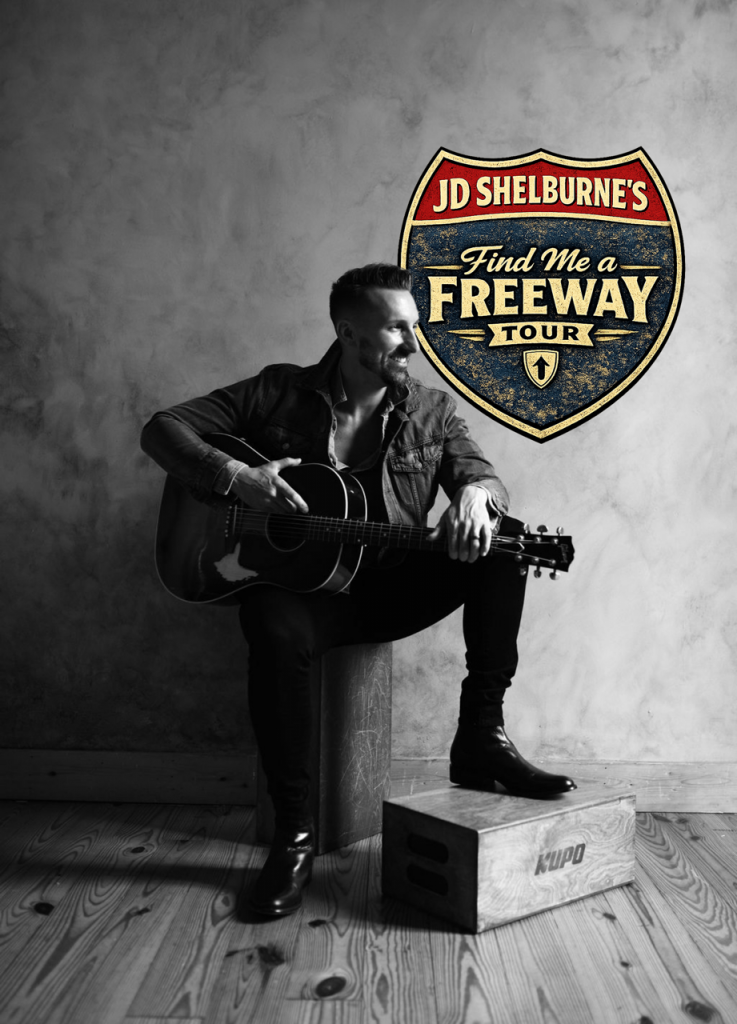 Black-and-white photo of a man sitting on a wooden crate, playing an acoustic guitar beside a vintage tour logo (Find Me a Freeway Tour).
