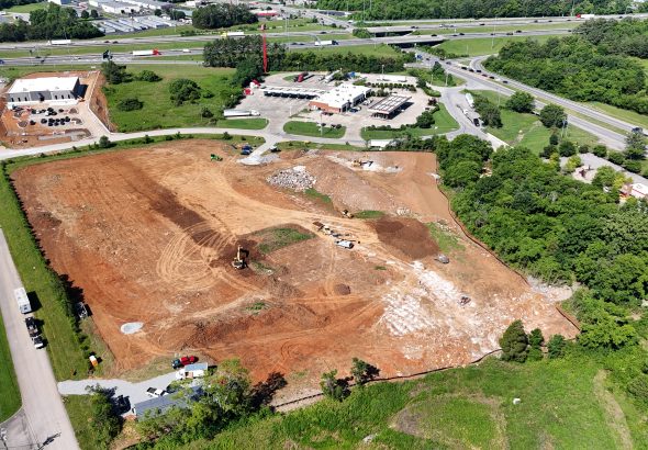 Aerial view of a large construction site with earthwork, excavators, and piles of dirt near roads and buildings.