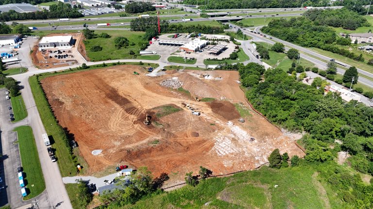 Aerial view of a large construction site with earthwork, excavators, and piles of dirt near roads and buildings.
