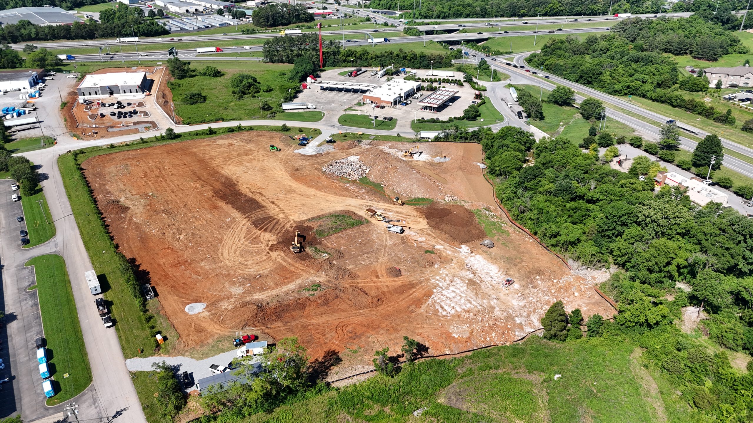 Aerial view of a large construction site with earthwork, excavators, and piles of dirt near roads and buildings.
