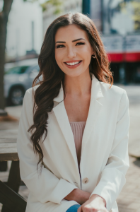Christina Sanjuan, meteorologist, smiling in a white blazer outdoors on an urban street; extol logo bottom-left.