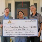 Three adults smile while holding a large donation check outside a brick building, addressed to Clark County Youth Shelter under a Community Foundation of Southern Indiana grant.